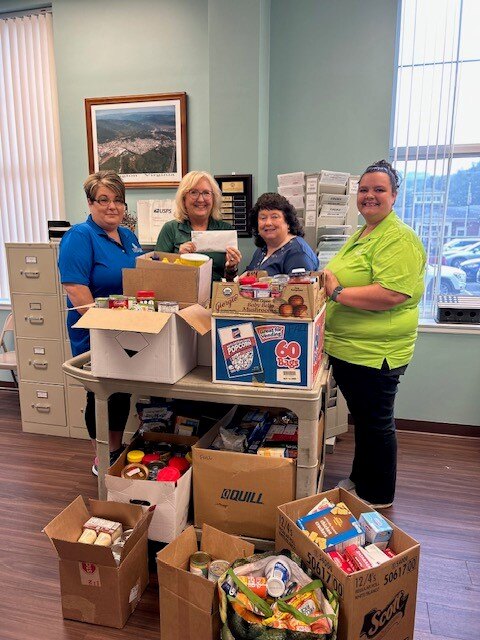 four women standing at a table covered with boxes of food donations and boxes on the floor with food donations
